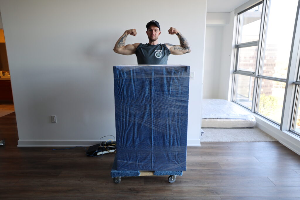 Qshark Moving Employee showing off his packing skills of a dresser and flexing muscles during a local move in Orange County. Double Drive Time Specialists